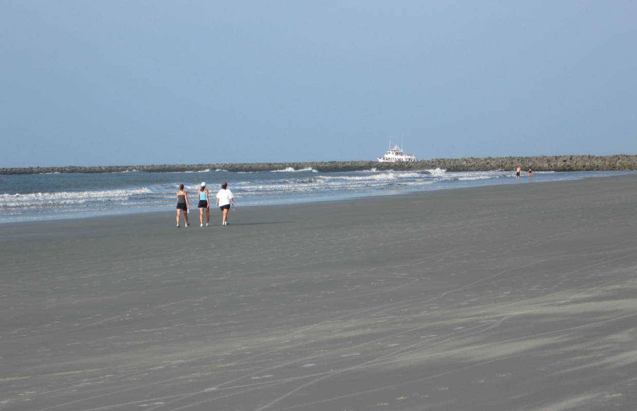 Wide stretch of beach with people, jetty and boat in distance at Bird Island Coastal Reserve at Sunset Beach