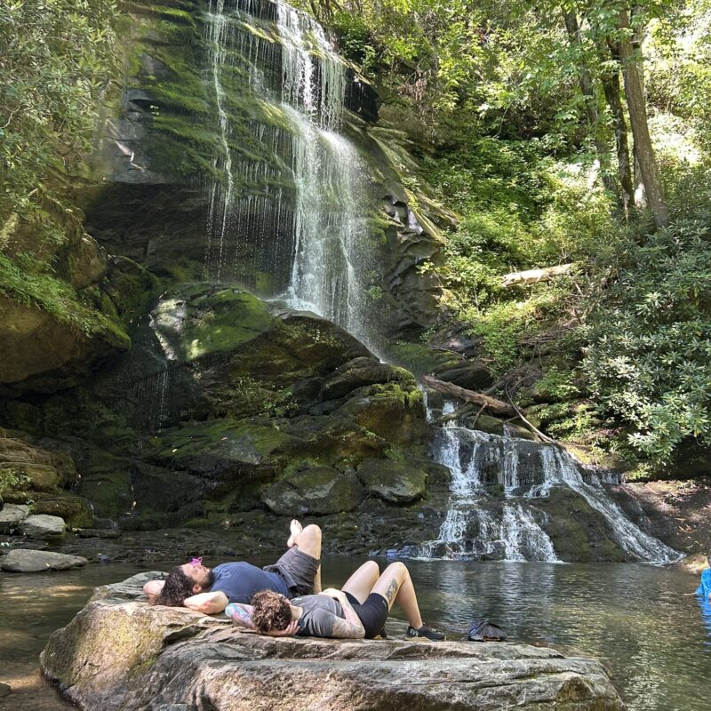 couple lying on rock at baseof waterfall in forest